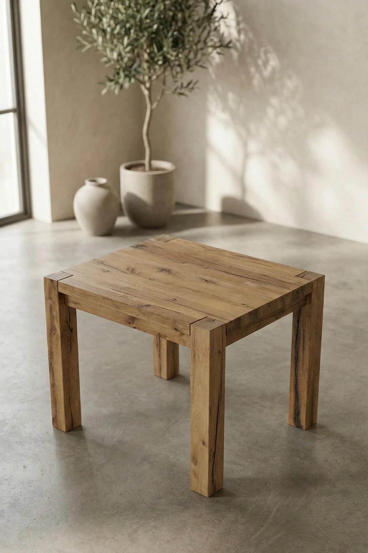 Wooden table in a room with a plant and vase on a concrete floor.
