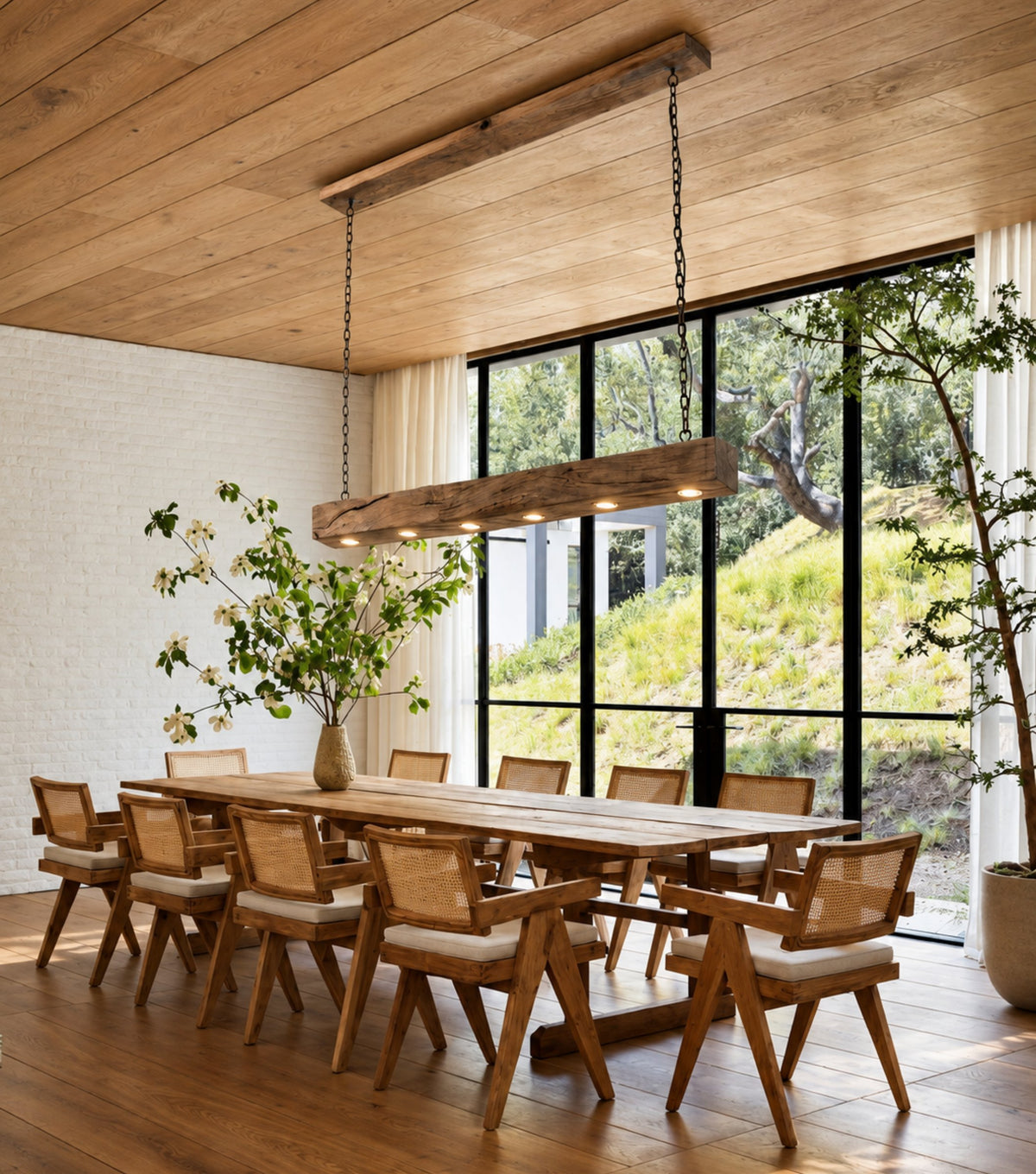 Lumen Reclaimed Chestnut Beam Pendant Light – above a long dining table with cane chairs